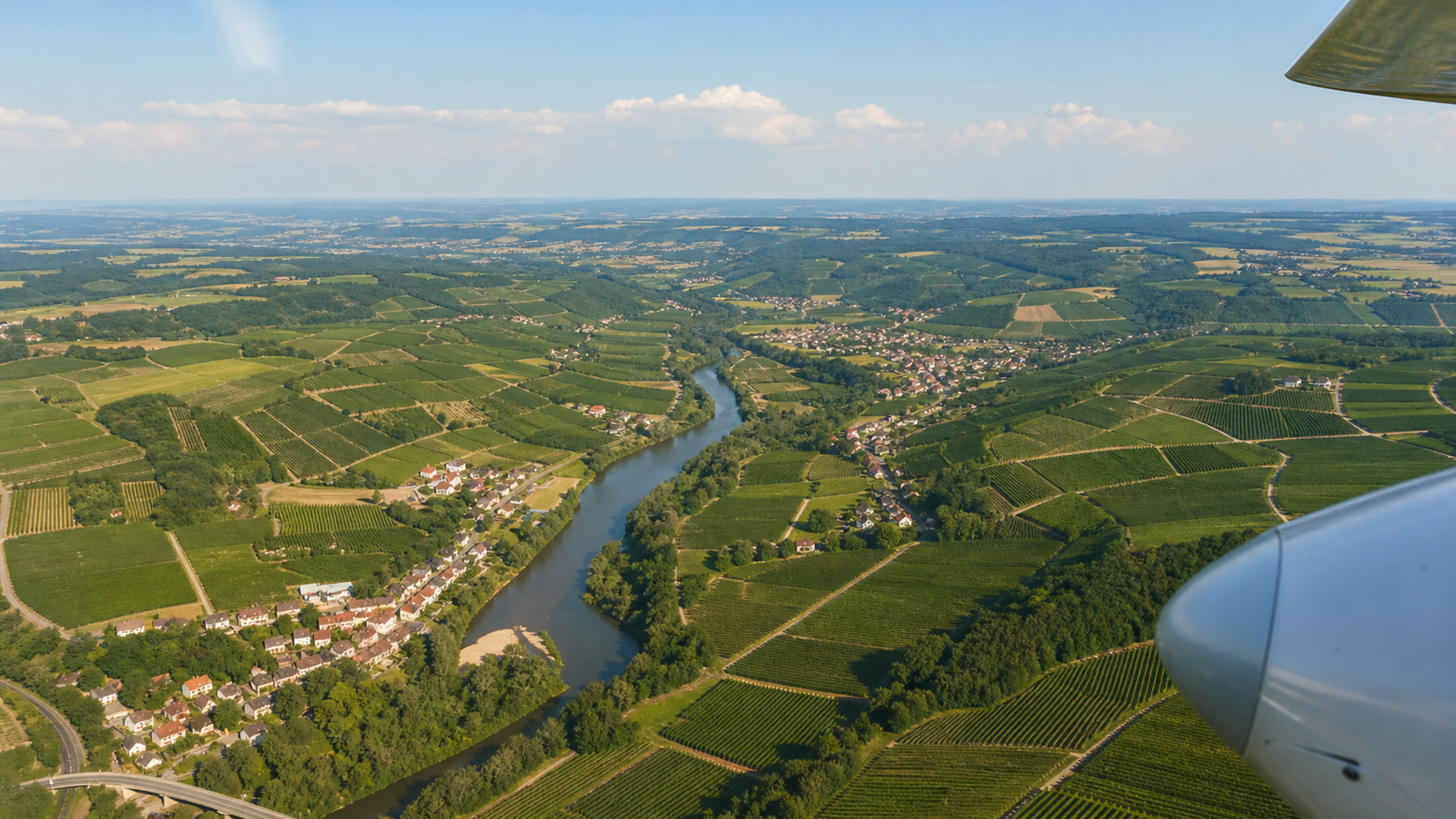 Luftaufnahme einer Hügellandschaft mit regelmäßigen Feldstrukturen und Flusslauf