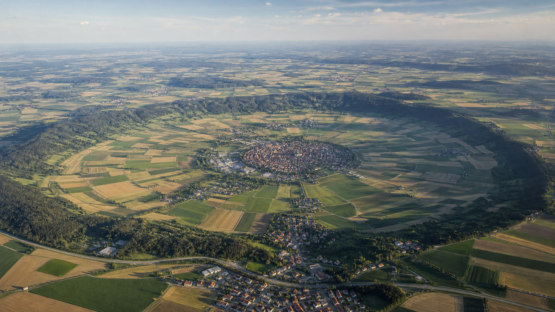 Luftaufnahme einer weiten, kreisförmigen Landschaftssenke mit Feldern und Ortschaften