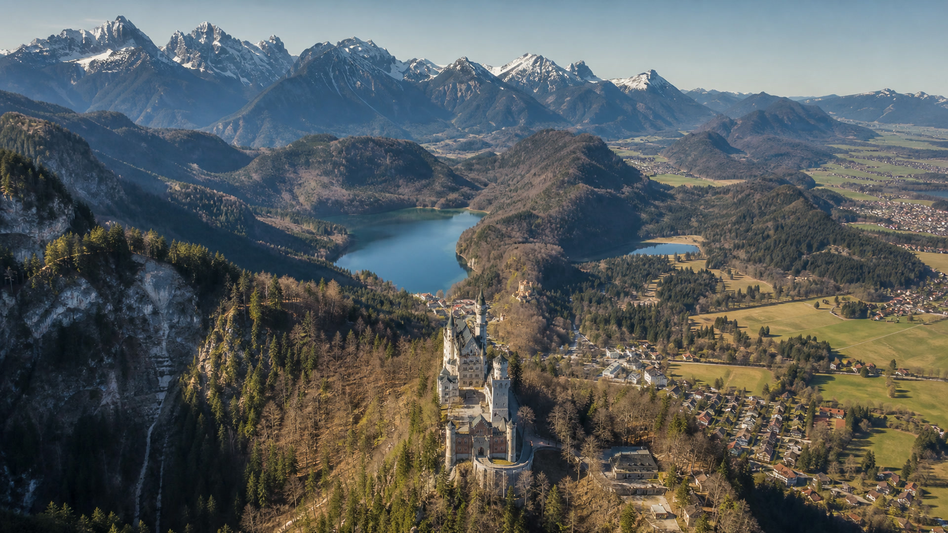 Luftaufnahme eines Schlosses auf einem bewaldeten Felsen vor Bergkulisse