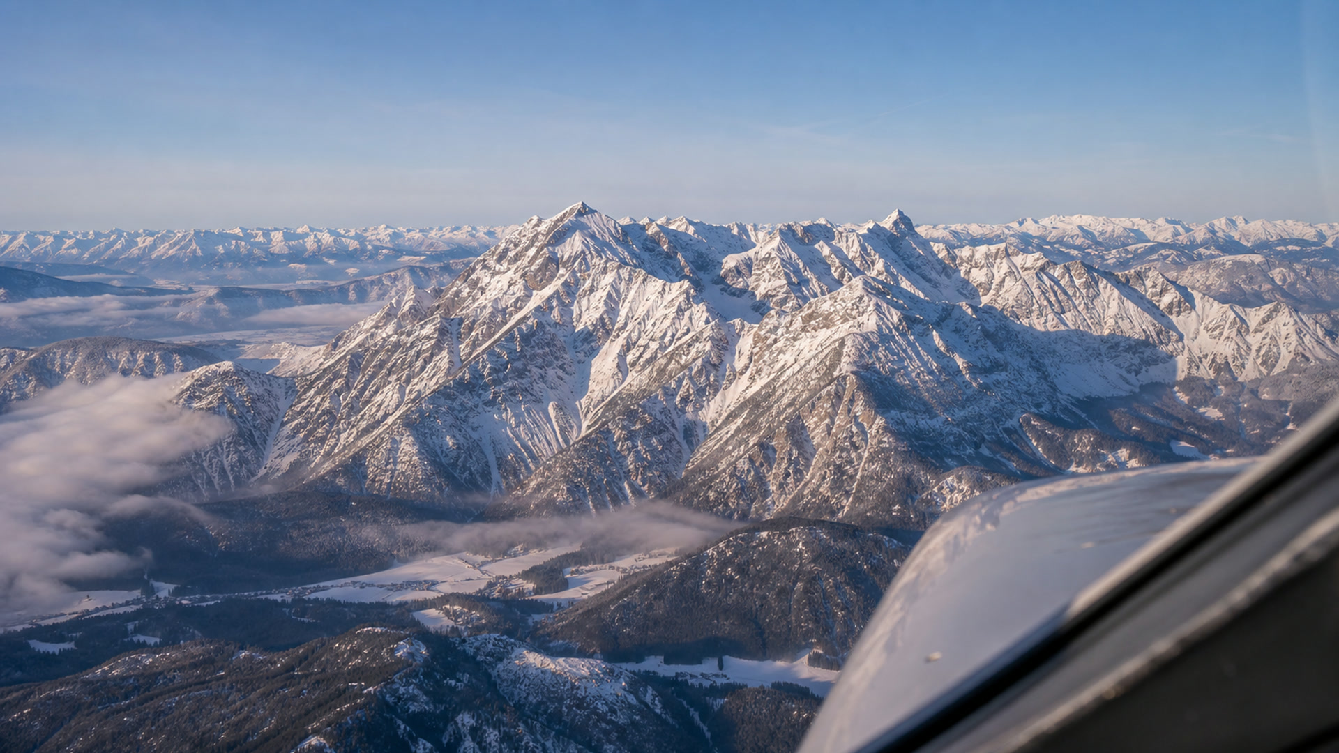 Luftaufnahme schneebedeckter Alpengipfel mit tief stehender Sonne