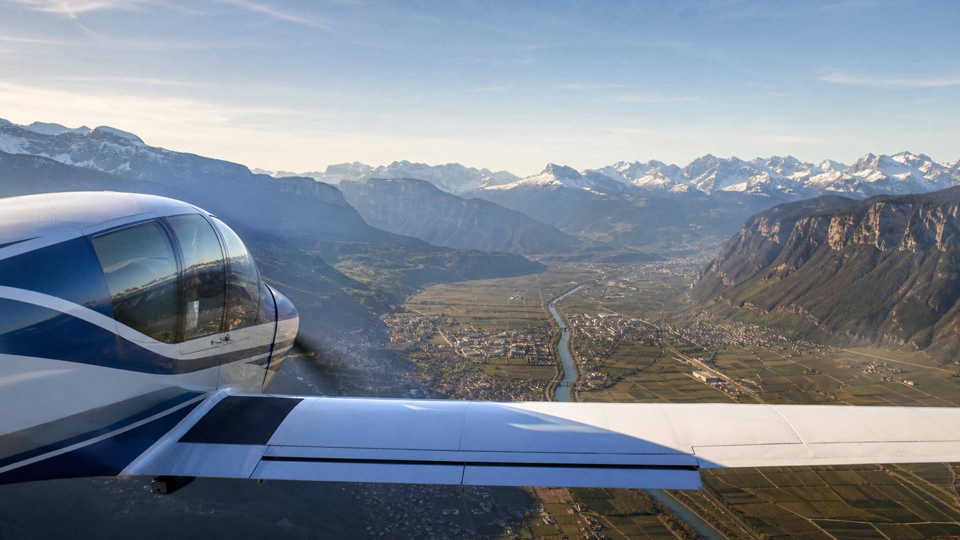 Flug über ein Alpental mit schneebedeckten Gipfeln zu beiden Seiten